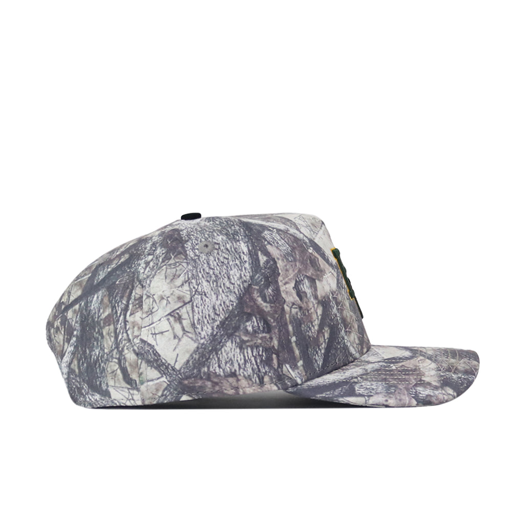 The Baylor Outland Hat by No Rivals is displayed in a side view, featuring a grey and brown leaf and branch camouflage pattern. This cap boasts a flat brim, structured crown, and an adjustable snap back closure. Made from high-quality cotton, it is finished with an embroidered No Rivals logo for added detail.