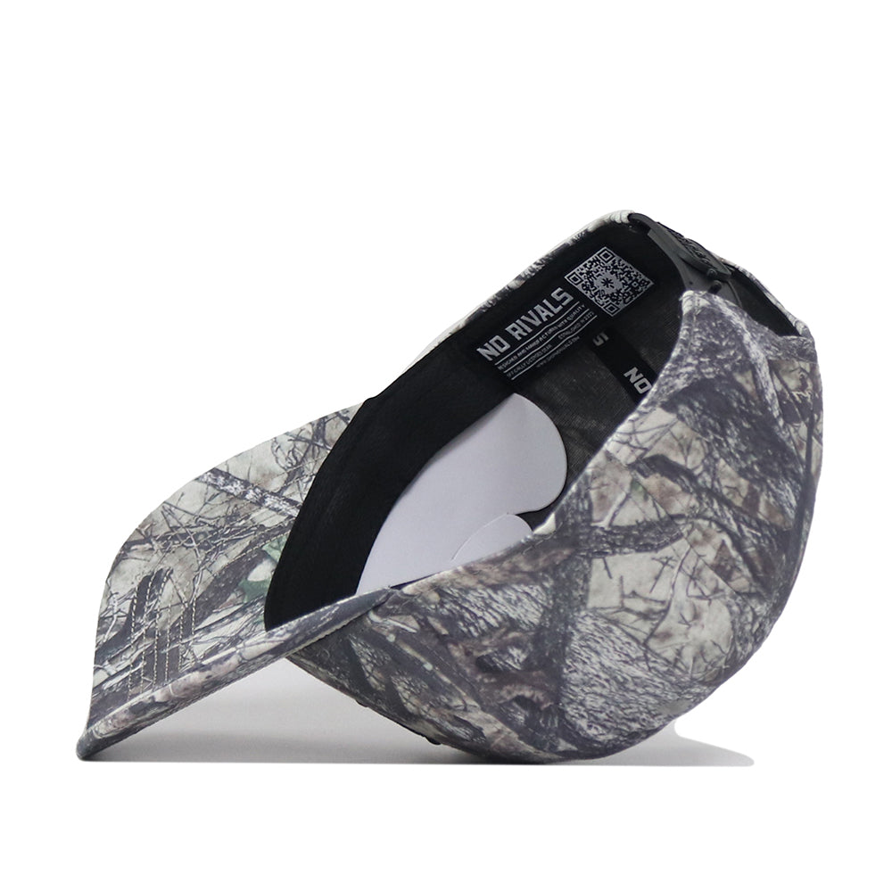 The Baylor Outland Hat by No Rivals is shown upside down, revealing an inside label that reads “NO RIVALS” and a QR code on the black internal band. Made from high-quality cotton, this cap features a grey and green camo pattern with a classic snapback closure.