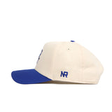 The No Rivals Creighton Logo Patch Hat is a cream cotton blend baseball cap with a blue bill and button, featuring 3D blue NR embroidery on the side.