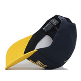 A Michigan Wolverines Boomerang Hat by No Rivals, in navy blue and yellow, is shown from the side with the brim facing left. The cap features an embroidered logo, a visible inner tag reading “NO RIVALS,” and a QR code on the inside band.