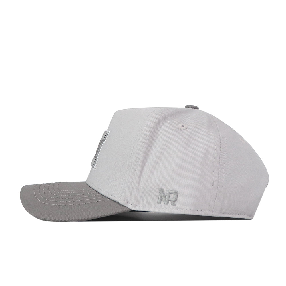 A side view of the Michigan Wolverines Graphite Hat by No Rivals shows its light gray design with a darker gray curved brim. The snap back closure provides a comfortable fit, while the embroidered NR initials near the back on the side add a subtle yet stylish brand detail.