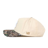 The No Rivals Michigan Wolverines Camo Connector Hat is a beige baseball cap made from high quality cotton, featuring a camouflage-patterned brim and gold NR initials on the side. Its snapback adjustment ensures a comfortable fit.