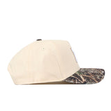 Side view of the No Rivals Michigan Wolverines Camo Connector Hat in beige, crafted from high-quality cotton and featuring a brown and green camouflage-patterned brim with an embroidered logo, displayed on a white background. This cap also offers a convenient snap back adjustment for a perfect fit.