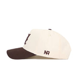 The No Rivals Alabama Espresso Hat features a cream snapback design with a dark brown brim, "NR" embroidered on the side, and is crafted from premium cotton. Shown in left side profile.