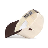 The Alabama Espresso Hat by No Rivals is a structured fit baseball cap in beige and brown, shown angled to reveal the interior with a NO RIVALS label, QR code near the sweatband, and crafted from premium cotton.