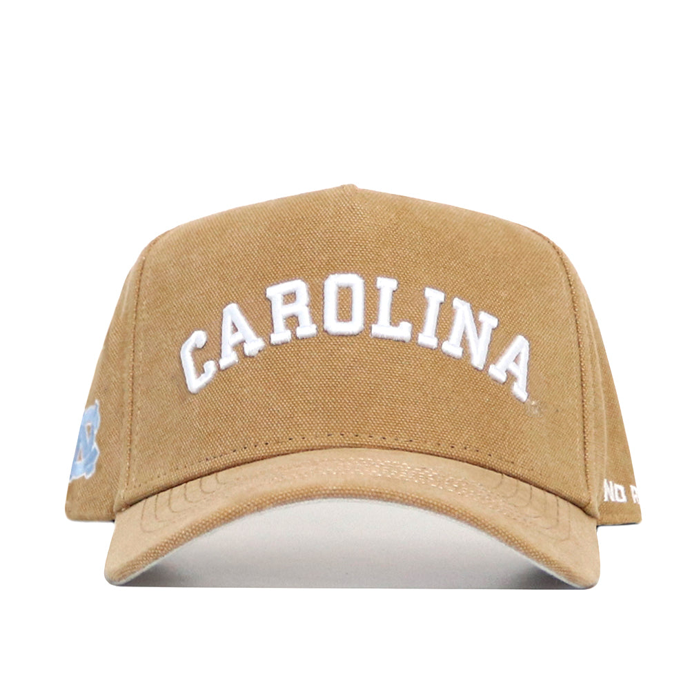 The No Rivals North Carolina Rustic Hat is a tan structured fit cap featuring "CAROLINA" embroidered in white on the front, with a small light blue logo on the left side. Made of classic cotton canvas.