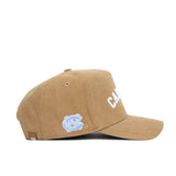 The No Rivals North Carolina Rustic Hat is a brown cotton canvas cap with a curved brim, white embroidered "C.A.R." on the front, and a light blue logo on the side. Displayed in a left side profile view, it offers a structured fit.