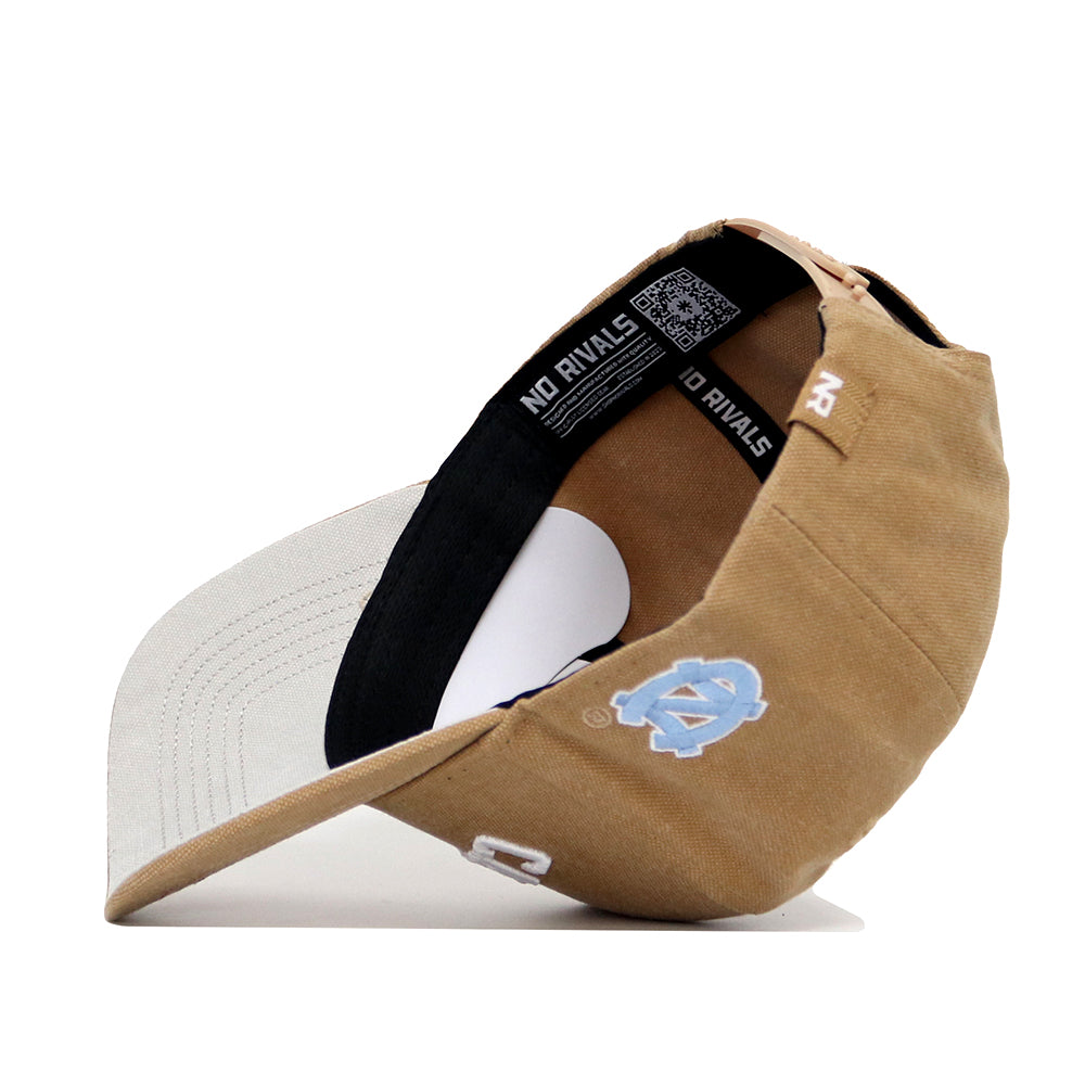 The North Carolina Rustic Hat by No Rivals features a tan and beige structured fit, a light blue North Carolina Tar Heels logo on the front, "NO RIVALS" on the black inner band, and a beige underside of the brim.