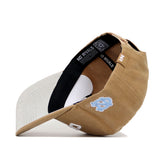 The North Carolina Rustic Hat by No Rivals features a tan and beige structured fit, a light blue North Carolina Tar Heels logo on the front, "NO RIVALS" on the black inner band, and a beige underside of the brim.