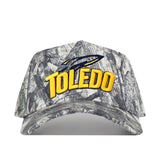 Introducing the Toledo Outland Hat by No Rivals—a camouflage structured fit hat featuring “TOLEDO” in yellow letters and a blue rocket logo embroidered on the front. This stylish embroidered cap is equipped with a convenient snap back adjustment, ensuring the perfect fit every time.