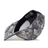 A No Rivals Toledo Outland Hat featuring a camo pattern and structured fit is shown flipped upside down, with its interior labels and black sweatband visible, as well as the snap back adjustment, while the brim rests on a white surface.