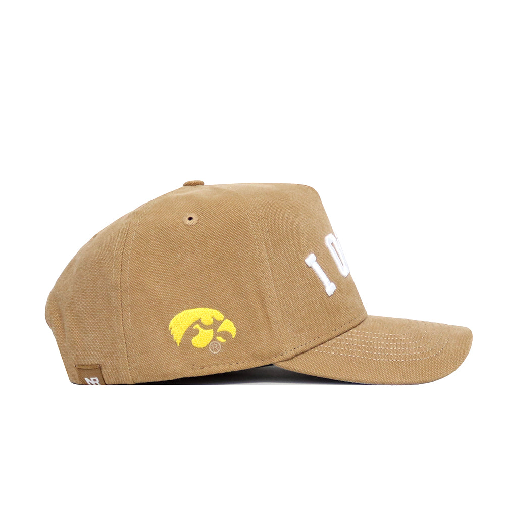 The Iowa Rustic Hat by No Rivals is a tan cotton canvas baseball cap featuring white embroidered letters on the front and a yellow Iowa Hawkeyes logo on the side. This officially licensed cap is shown from the left side.