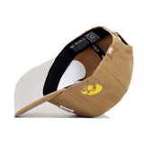The Iowa Rustic Hat by No Rivals is a tan cotton canvas baseball cap flipped inside out, revealing a black inner band with NO RIVALS text, white paper insert, yellow bird graphic outside, and an adjustable snapback for comfort.