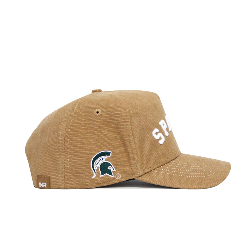 Side view of the No Rivals Michigan State Rustic Hat in brown cotton canvas with white stitching, featuring "SPARTANS" partially visible and a green and white Spartan helmet logo on the side. Structured fit with snapback adjustment.