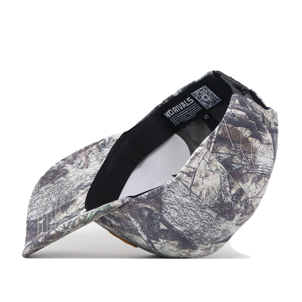 The No Rivals Mizzou Outland Hat is shown on its side, revealing the underside of the bill and the inside label with text and a QR code. This camouflage baseball cap features a structured fit for comfortable wear, combining style and practicality.