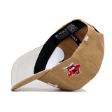 The Western Kentucky Rustic Hat by No Rivals is shown upside down, revealing its inner band and tags. This tan and white cotton canvas cap features an embroidered red cartoon character with a white outline and black details on the side.