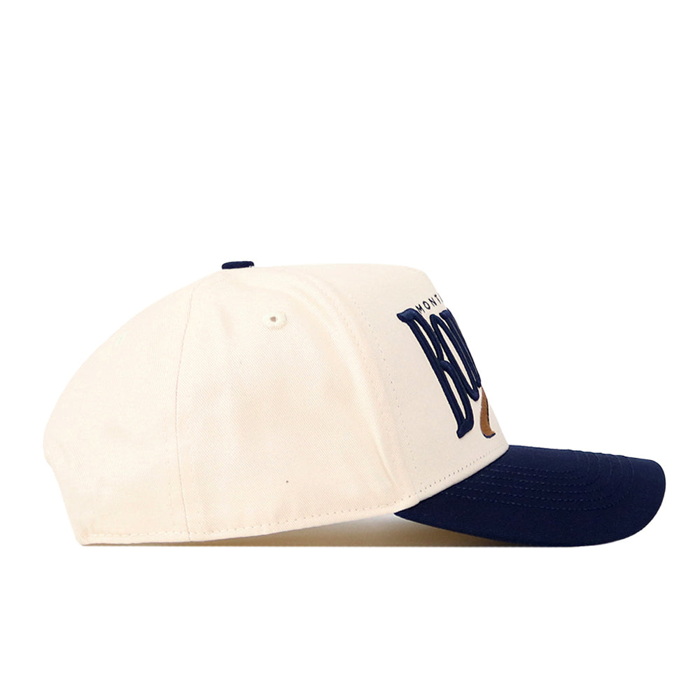 The No Rivals Montana State Bobcats Stride Hat features a cream-colored snapback design with a navy blue brim and partially visible navy blue embroidered logos on the front, shown in a side profile view against a white background—the perfect addition to your gameday fit.
