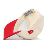 A beige and red officially licensed No Rivals Wisconsin Patch Hat is displayed upside down, showcasing its inner lining, stitching, and labels. The hat features a small embroidered M logo on the side near the brim and is equipped with a classic snap back closure for an adjustable fit.