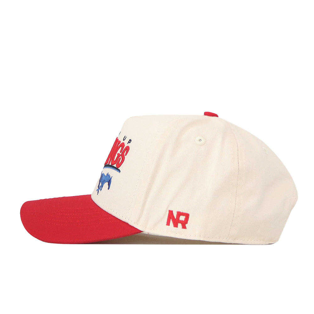 The No Rivals SMU Mustangs Stride Hat is a cream snapback baseball cap featuring a red brim. The side displays red embroidered “NR” initials, while the front showcases officially licensed SMU Mustangs graphics and text in red and blue, partially visible from this angle. Detailed embroidered logos complete the authentic look.