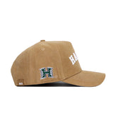 The No Rivals Hawaii Rustic Hat is a tan cotton canvas cap with white stitching, “HAWAII” in white on the front, a green “H” logo on the side, curved brim, and an “NR” side tag.
