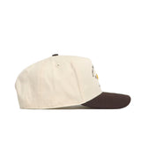 A side view of the No Rivals Iowa State Outlaw Hat - Classic, featuring a cream color, dark brown brim, snapback closure, top button, stitched eyelets, and an embroidered logo against a white background.