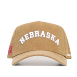 Front view of the Nebraska Rustic Hat by No Rivals, a tan cotton canvas cap with "NEBRASKA" in large white letters on the front, a red N logo on the left side, and a structured fit design.