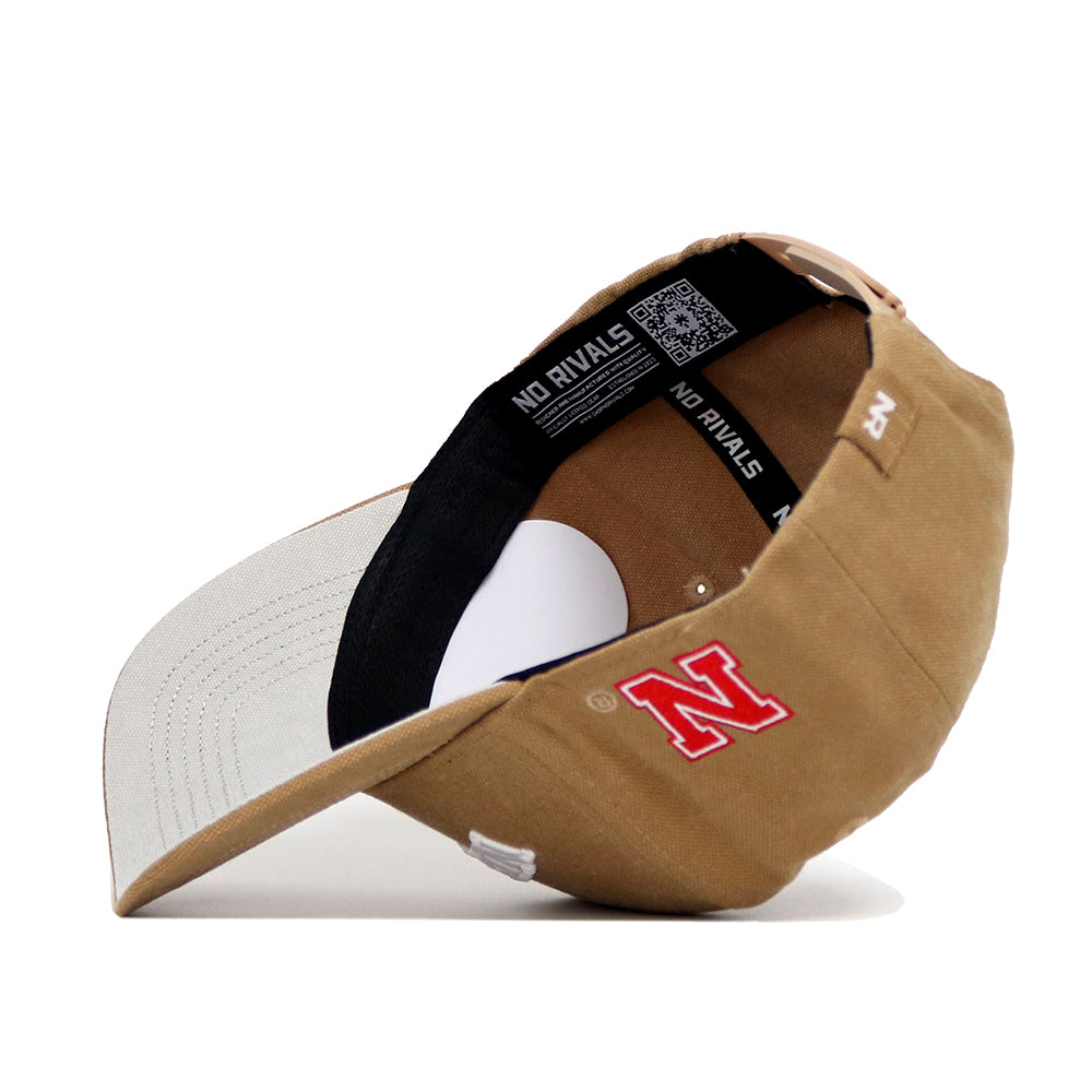 The Nebraska Rustic Hat by No Rivals is a tan cotton canvas baseball cap with a red embroidered N on the front, NO RIVALS inside label, snapback closure, and light gray underside brim for classic style.