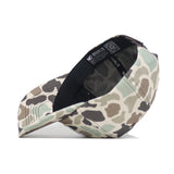 A side view of the Nevada Huntsman Hat by No Rivals, a 5-panel camo baseball cap in green, brown, and beige with an inner sweatband, adjustable snapback strap, and "NO RIVALS" printed inside.