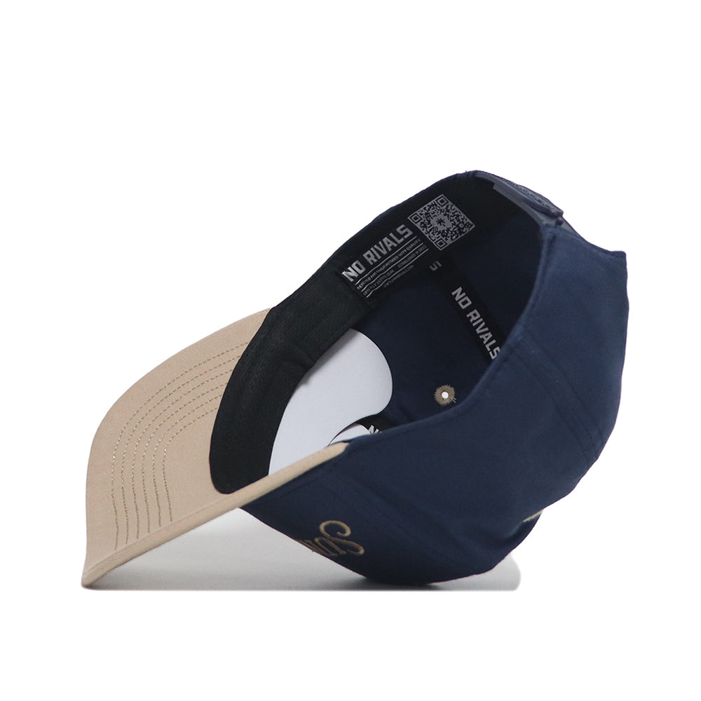 The Sunday Golf Hat by No Rivals is shown upside down, revealing the inside lining and NO RIVALS branding on the inner band. The underside of the navy and tan brim features beige fabric with visible stitching—ideal for gameday style.