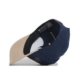 The Sunday Golf Hat by No Rivals is shown upside down, revealing the inside lining and NO RIVALS branding on the inner band. The underside of the navy and tan brim features beige fabric with visible stitching—ideal for gameday style.