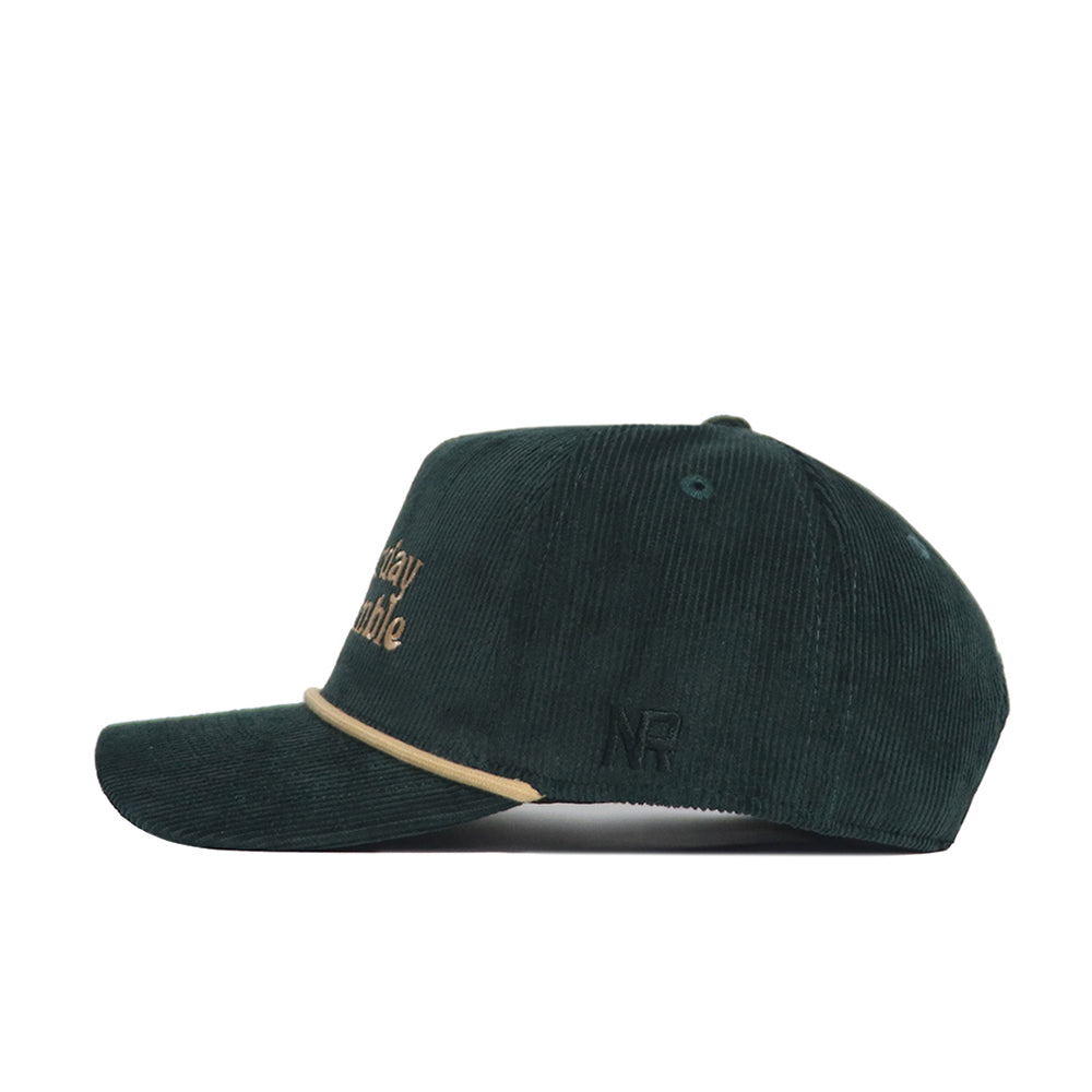 The No Rivals Saturday Scramble Cord Hat in dark green cotton corduroy features beige embroidered logos on the front and a beige trim above the brim, shown from a left side profile view.