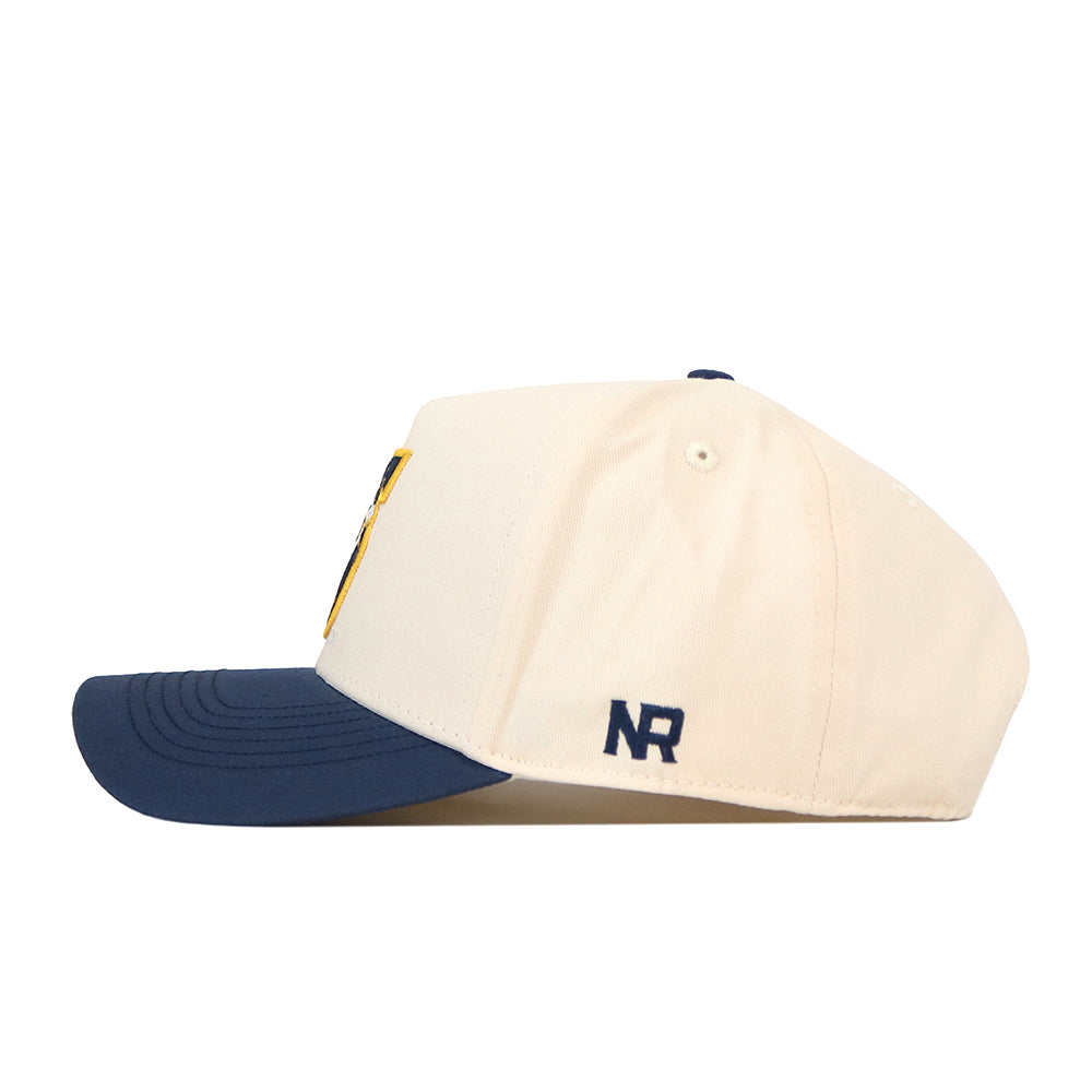 A side view of the WVU Pat White’s No. 5 Hat - Classic Navy by No Rivals, featuring a cream-colored crown and a navy blue bill. The NR initials are embroidered in navy on the side, and the cap is designed with a snap back closure for adjustable comfort. An embroidered logo adds an extra touch of style to this sporty cap.
