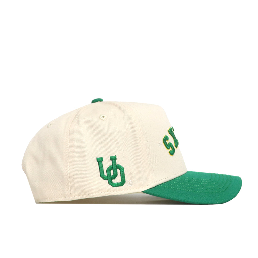 The No Rivals Upside Down Ducks Hat - Oregon - Classic is a cream snapback with a green brim, made from quality cotton. It features green and yellow embroidered UO letters on the side and partially visible text on the front.