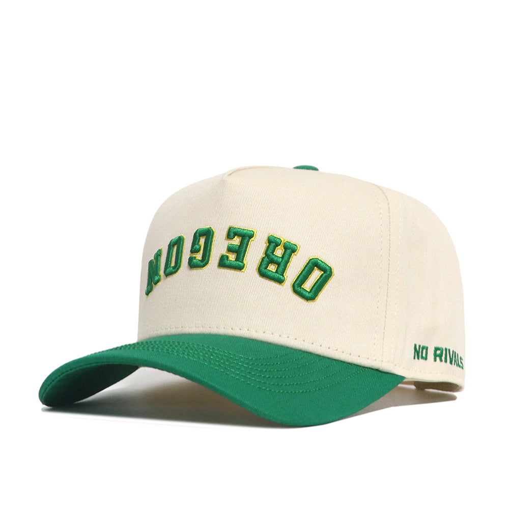 The Upside Down Oregon Hat - Classic by No Rivals is a cream snapback with a green brim. OREGON is embroidered upside down in green and yellow on the front, NO RIVALS on the side. Includes an embroidered logo and is officially licensed.