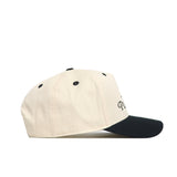 The No Rivals Play Golf Hat - Teed Up - Classic Black is shown in side profile on a white background, featuring a beige crown, black curved brim and eyelets, plus an embroidered logo.
