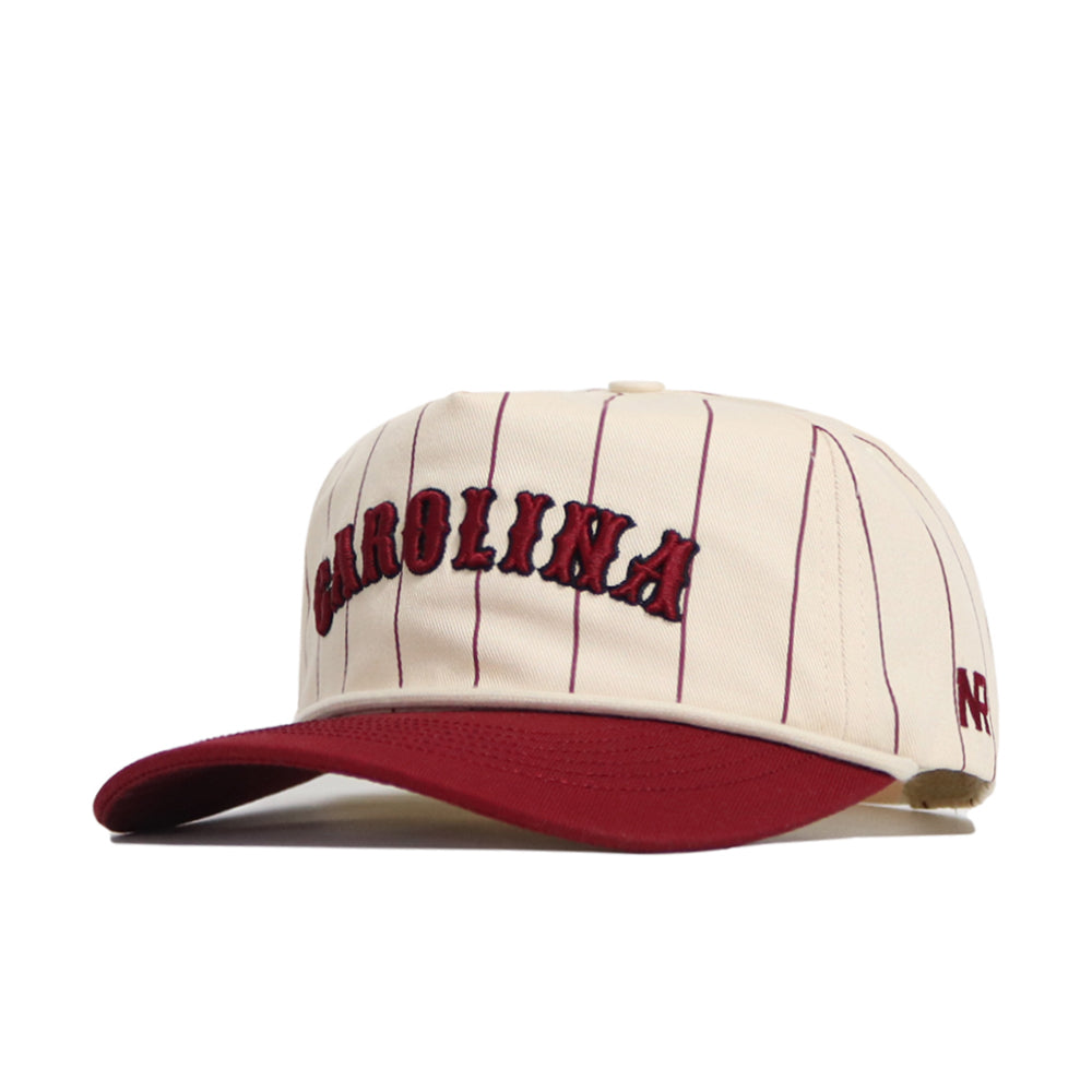 The No Rivals South Carolina Walk Off Hat is a cream cotton cap with thin maroon pinstripes, an unstructured fit, "CAROLINA" embroidered in maroon on the front, a maroon brim, and "NC" stitched on the side.