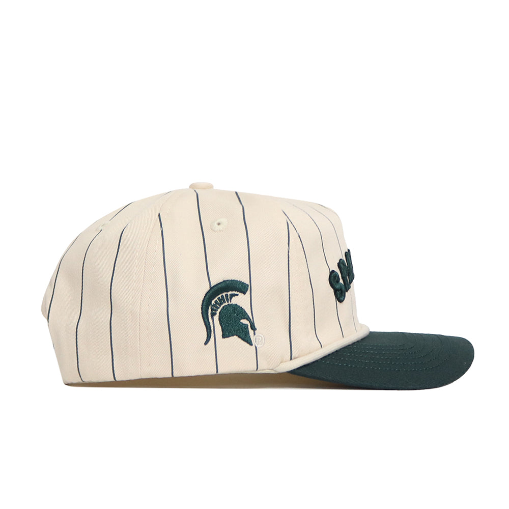 The No Rivals Michigan State Walk Off Hat features cream cotton fabric with black pinstripes, a dark green brim, and an embroidered Spartan helmet logo. It has an adjustable snap back closure for a comfortable fit.