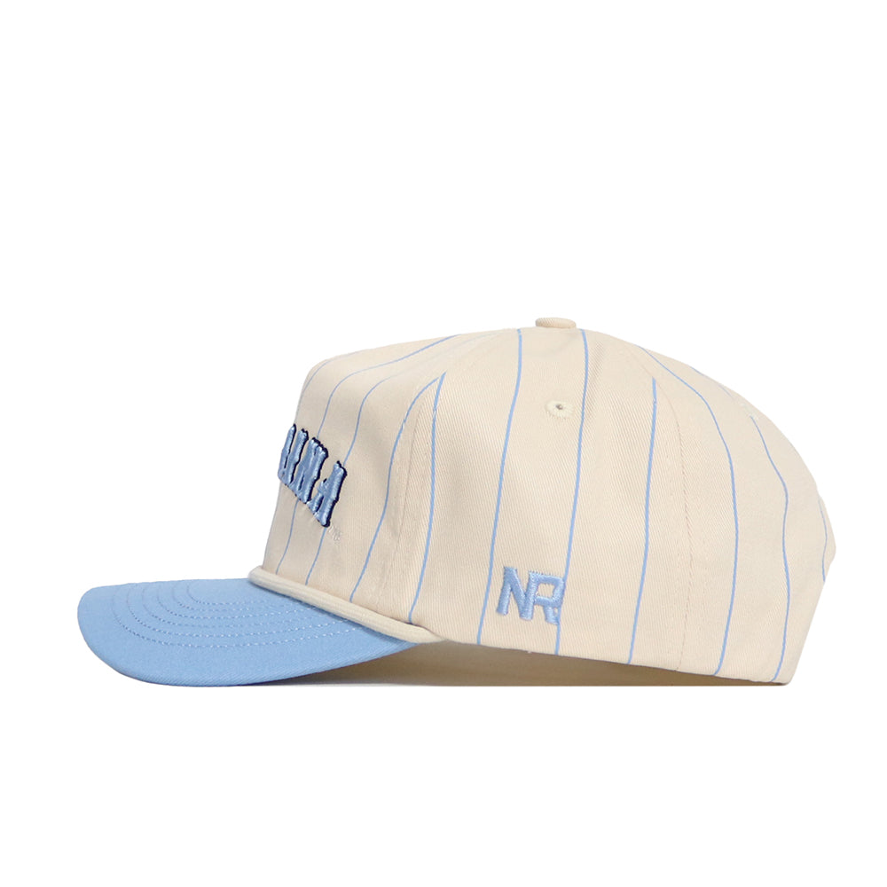 The No Rivals North Carolina Walk Off Hat is a cream snapback with thin blue stripes, a light blue brim, raised blue front lettering, and embroidered NR initials on the side. Made from high-quality cotton.