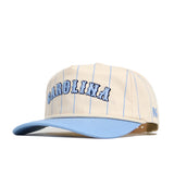 The No Rivals North Carolina Walk Off Hat is a beige cotton baseball cap with thin blue pinstripes, large CAROLINA embroidery, a light blue brim, an unstructured fit, and a small blue N logo on the side.