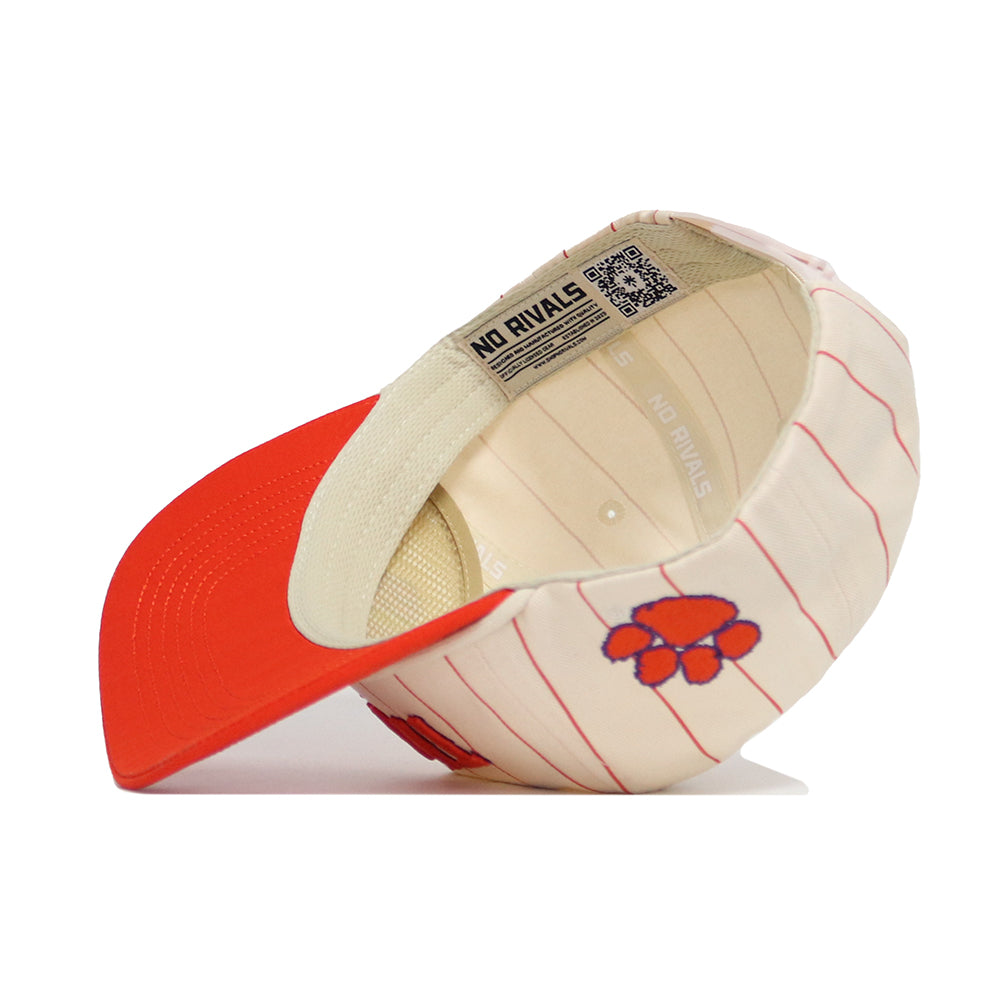 The Clemson Walk Off Hat by No Rivals is a cream snapback with red pinstripes, an orange brim, and an orange paw print logo. Shown upside down, its interior displays a "NO RIVALS" label. Made from high-quality cotton.