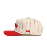 The No Rivals Nebraska Walk Off Hat is a cream-colored cotton cap with thin red pinstripes, a solid red brim, and red embroidered NR on the side. Its adjustable design ensures comfort and style for any head size.