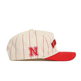 The No Rivals Nebraska Walk Off Hat is a cream cotton snapback with vertical red pinstripes, a red brim, a side N logo, and partially visible red front lettering. Officially licensed, it blends style and comfort.