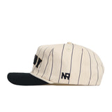 The Vanderbilt Walk Off Hat by No Rivals features cream-colored cotton with thin black stripes, a black brim, and NR embroidered above the brim. Its soft fabric ensures a comfortable, unstructured fit.