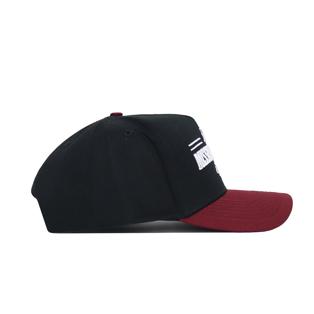 The Mississippi State Tailgate Hat by No Rivals is a snapback with a black crown and dark red brim, made from high-quality cotton. Side view shows its structured fit and white embroidered text on the front; words are partially obscured.