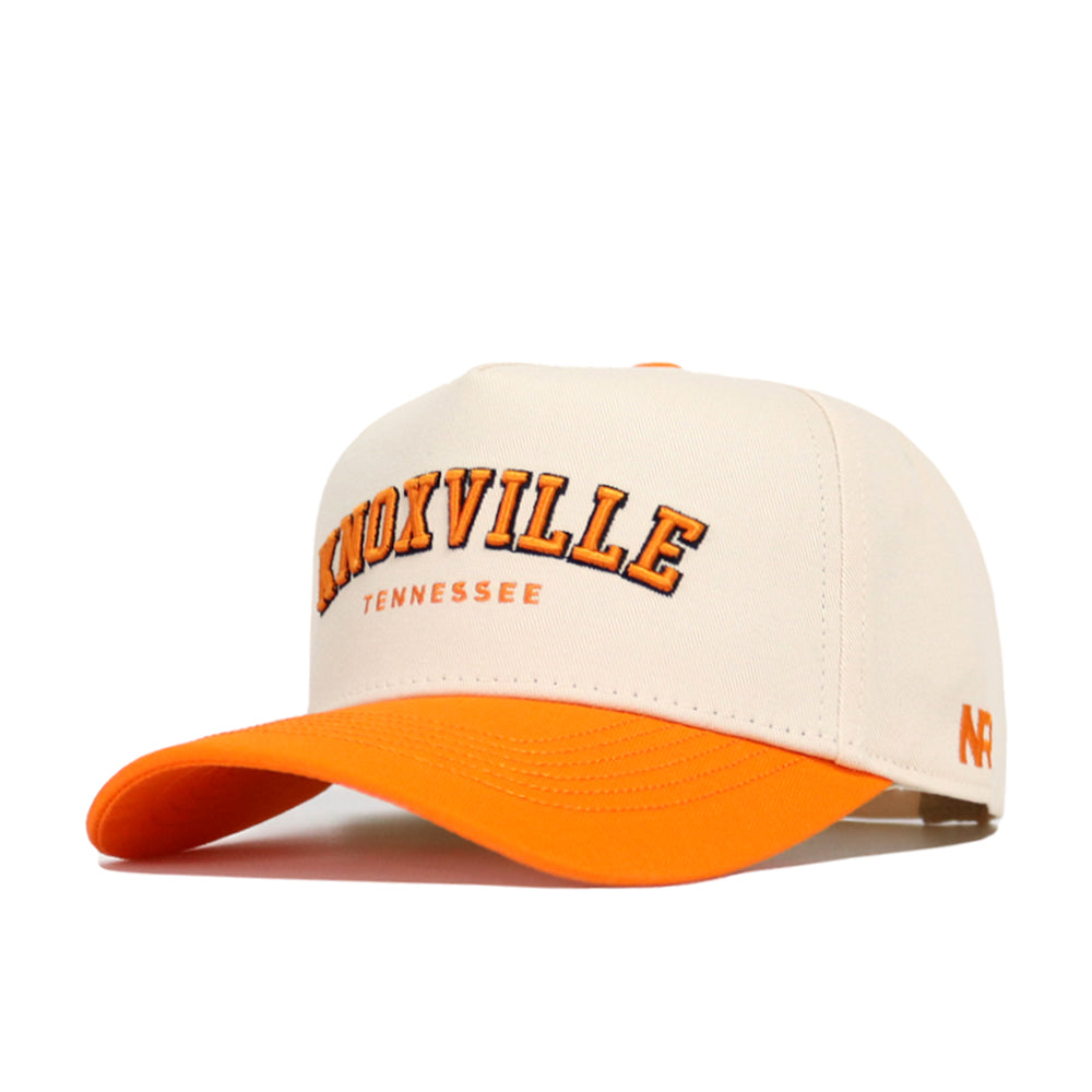 The No Rivals Knoxville Hometown Hat is a cream cotton baseball cap with an orange brim, featuring bold "Knoxville" and "Tennessee" embroidery, an orange NR logo on the side, and a snapback closure for adjustable fit.
