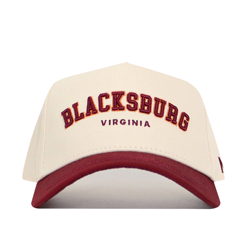The Blacksburg Hometown Hat by No Rivals is a cream cotton cap with a maroon brim, featuring “BLACKSBURG” in maroon and gold and “VIRGINIA” below. Its snapback design ensures a structured, comfortable fit.