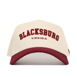 The Blacksburg Hometown Hat by No Rivals is a cream cotton cap with a maroon brim, featuring “BLACKSBURG” in maroon and gold and “VIRGINIA” below. Its snapback design ensures a structured, comfortable fit.