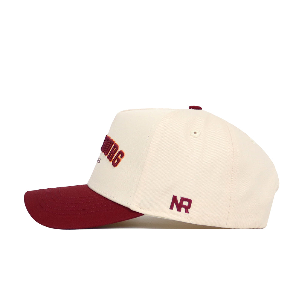 The No Rivals Blacksburg Hometown Hat is a cream snapback with a maroon brim, maroon NR logo on the side, and partially visible maroon and gold embroidery on the structured cotton front.
