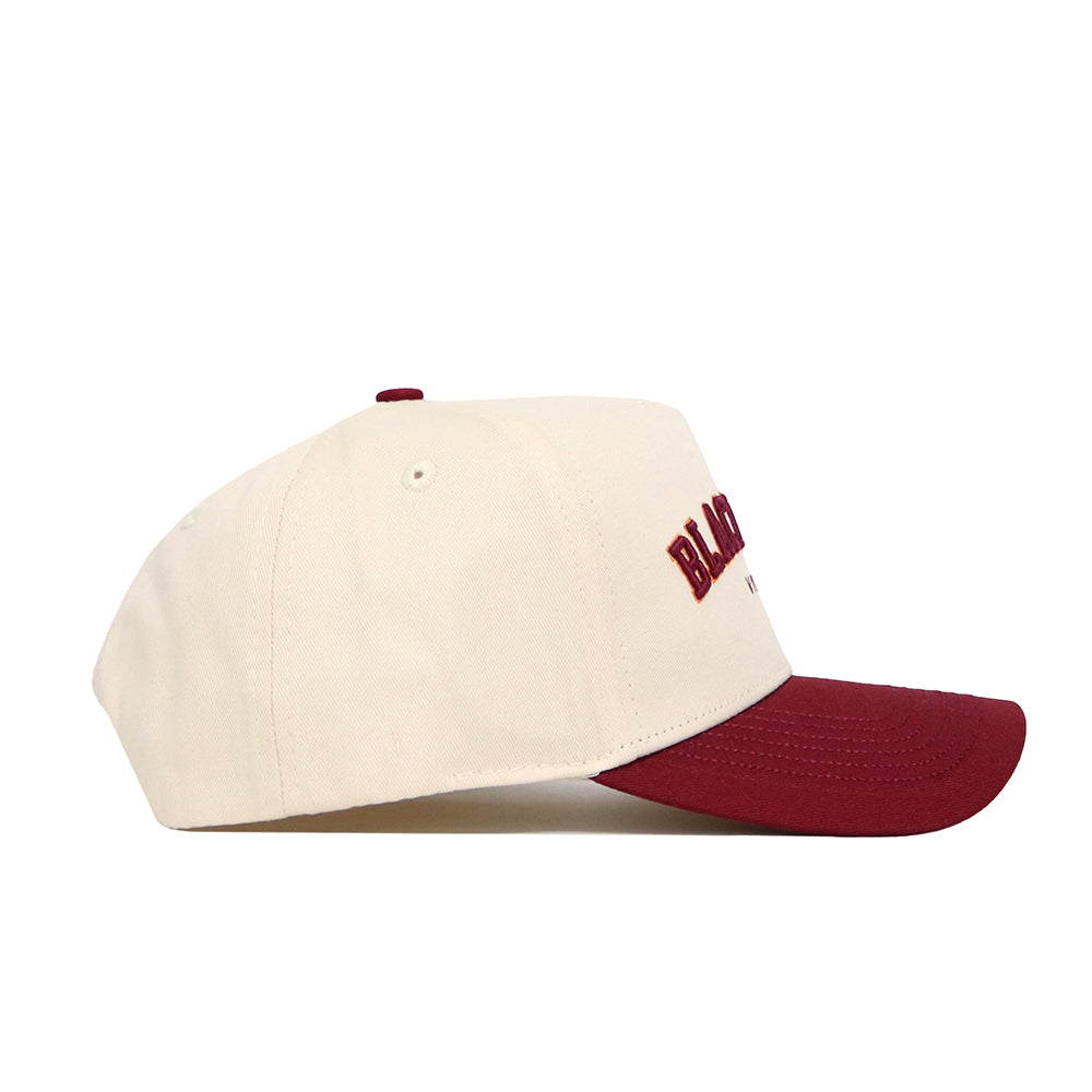 The No Rivals Blacksburg Hometown Hat is a cream snapback with a maroon brim and front embroidery, made from premium cotton, displayed side-on against a white background.