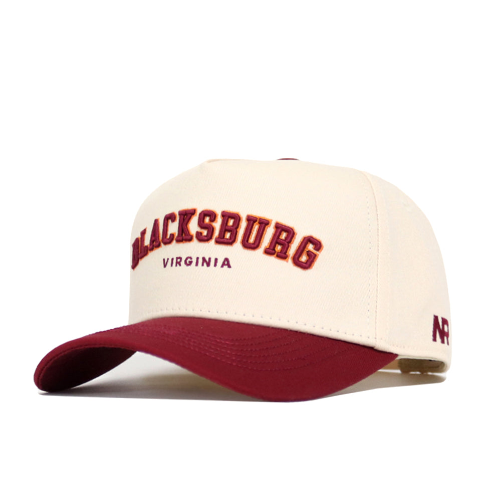 The Blacksburg Hometown Hat by No Rivals is a cream snapback with a maroon bill, made from premium cotton. It features "BLACKSBURG" in maroon and gold embroidery, with "VIRGINIA" stitched below in smaller maroon lettering.